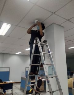 Teknisi memasang perangkat jaringan di plafon area kantor.